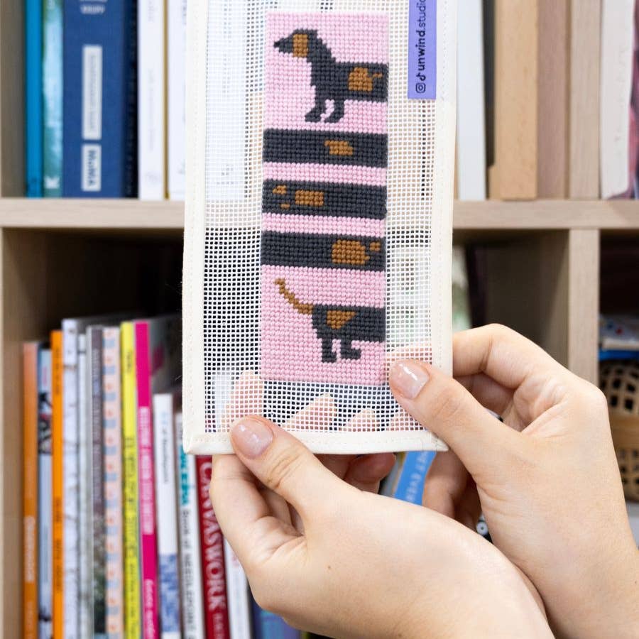 Sticken-auf-Stramin-Lesezeichen mit schwarz-braunem Dackelmotiv auf staubrosa Stoff in einem geöffneten Buch