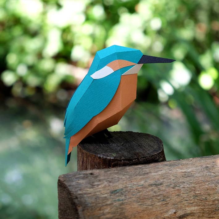 Papier-Eisvogel an einer Möbelkante mit nach außen hängendem Schwanz